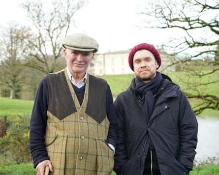 A man with a flat cap and a beige checked waistcoat with a younger man wearing a red beanie and a black overcoat.
