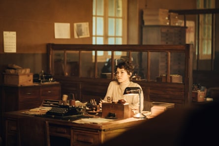 Ross, in early 20th-century dress, stares across a desk and over a typewriter.
