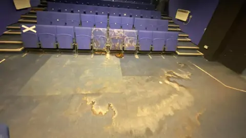 Nottingham New Theatre A small theatre auditorium, showing front row seats and some carpeted floor badly stained by water