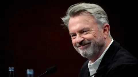 Reuters Sam Neill smiles against a black background, at the San Sebastian Film Festival in Spain in 2019