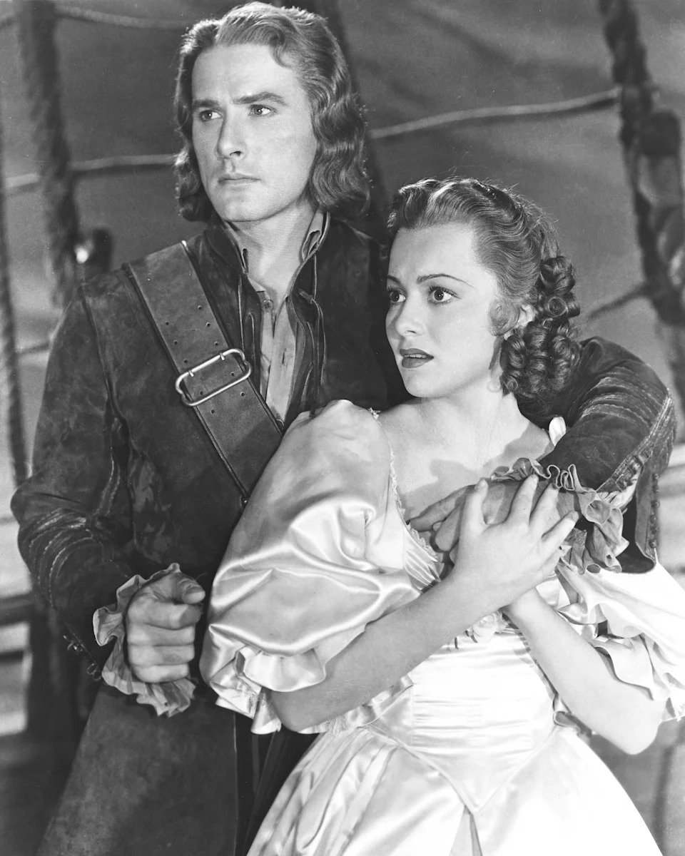 Errol Flynn and Olivia de Havilland in historical costumes on a ship set